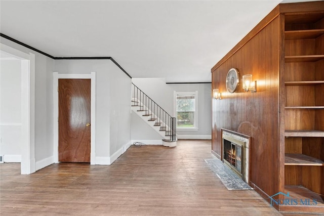 unfurnished living room with a fireplace with flush hearth, wood finished floors, ornamental molding, baseboards, and stairs