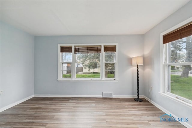 spare room with wood finished floors, a wealth of natural light, baseboards, and visible vents