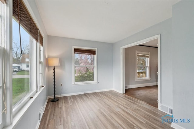 empty room with wood finished floors, visible vents, and baseboards