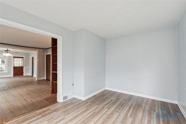 spare room with wood finished floors, visible vents, a ceiling fan, and baseboards