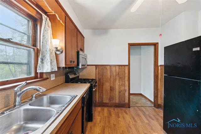 kitchen with a sink, wainscoting, black appliances, brown cabinets, and light wood-style floors