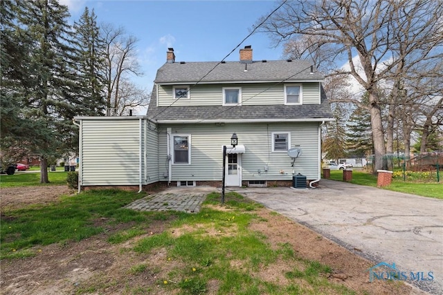 rear view of property with a patio area, a chimney, a lawn, cooling unit, and roof with shingles