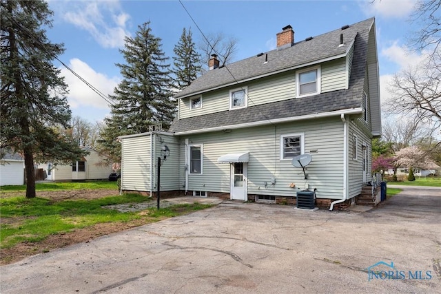 back of property with a shingled roof and a chimney