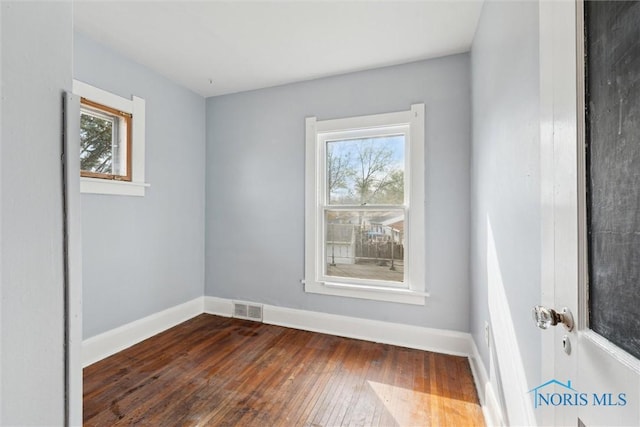 empty room with dark wood finished floors, baseboards, and visible vents