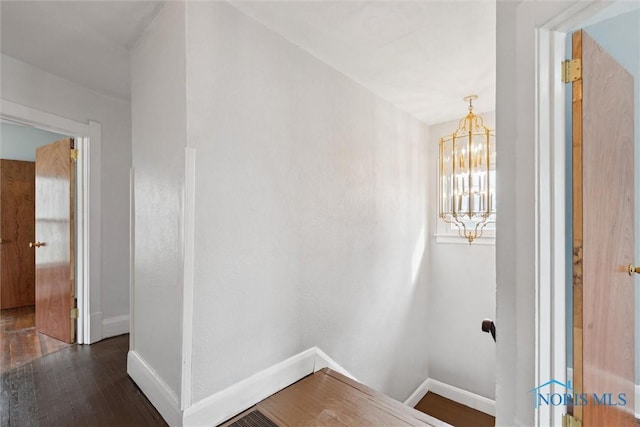 corridor featuring baseboards, a notable chandelier, and wood finished floors