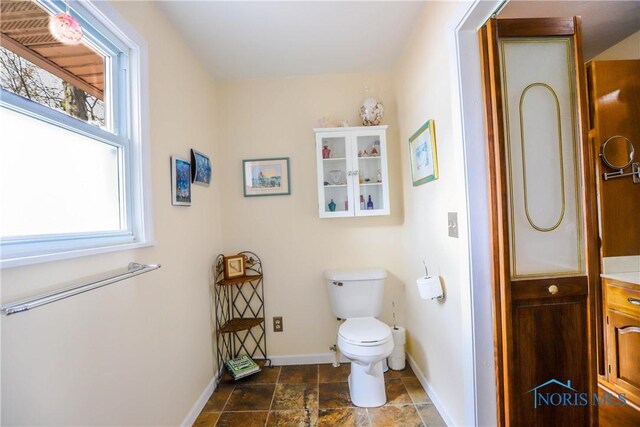 bathroom featuring baseboards, toilet, and stone finish flooring