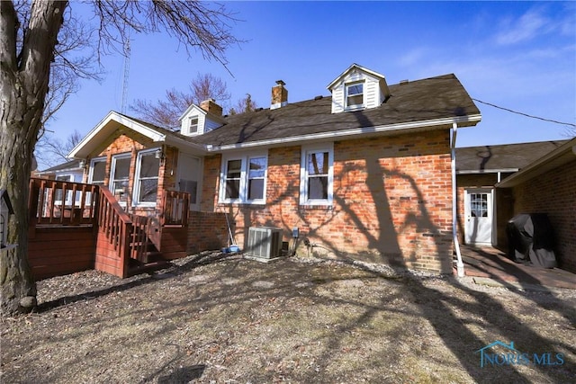 rear view of property with brick siding, central air condition unit, and a chimney