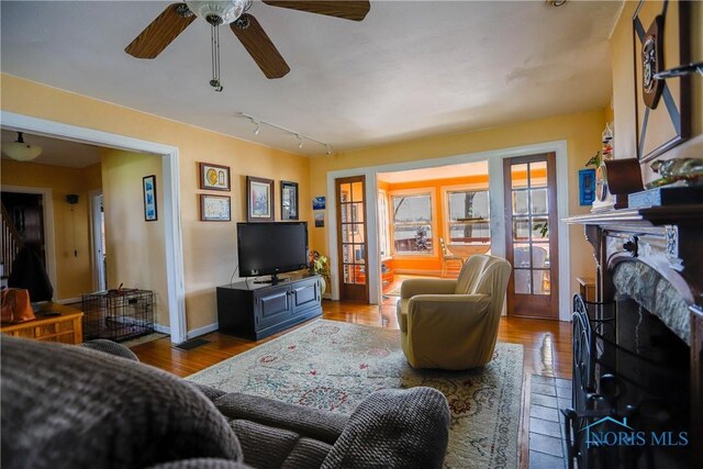living room featuring rail lighting, baseboards, a ceiling fan, a fireplace, and wood finished floors