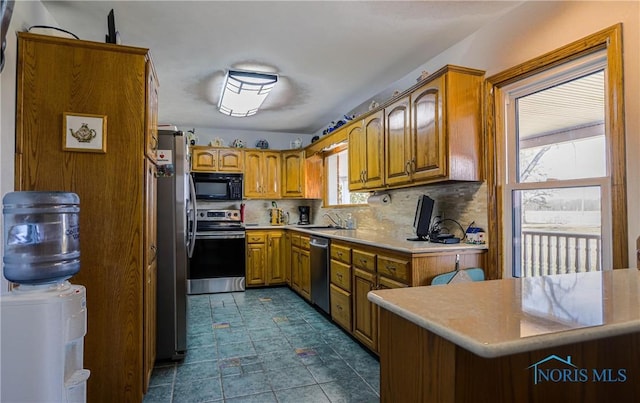 kitchen featuring light countertops, a sink, brown cabinetry, stainless steel appliances, and decorative backsplash