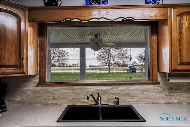 kitchen featuring decorative backsplash, light countertops, a sink, and ceiling fan