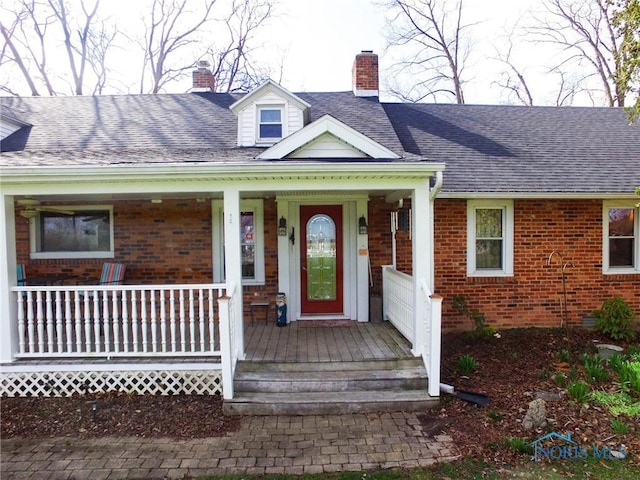 doorway to property featuring a chimney, covered porch, and brick siding