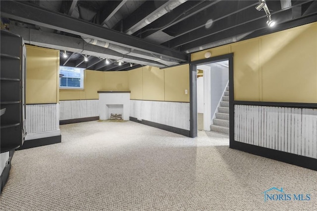below grade area with a wainscoted wall, carpet floors, track lighting, and stairs