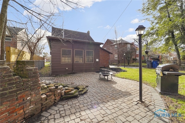 rear view of property featuring a patio area, roof with shingles, an outdoor fire pit, fence, and a yard