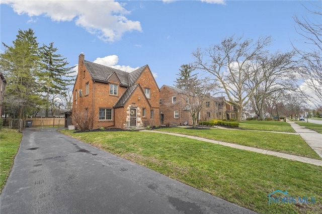 tudor house with a front lawn, a chimney, fence, and brick siding