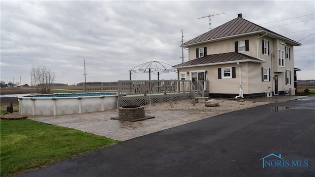 exterior space with a standing seam roof, a wooden deck, metal roof, an outdoor fire pit, and a fenced in pool