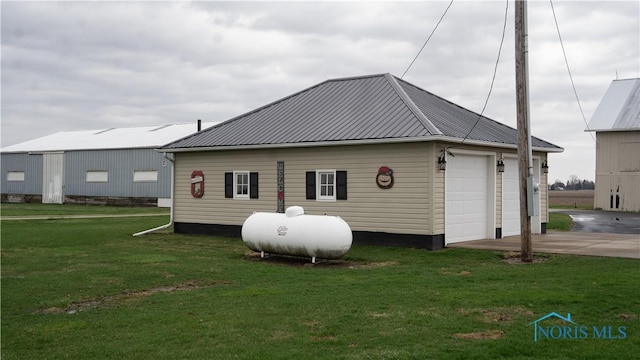 rear view of house featuring concrete driveway, an outdoor structure, metal roof, a garage, and a yard