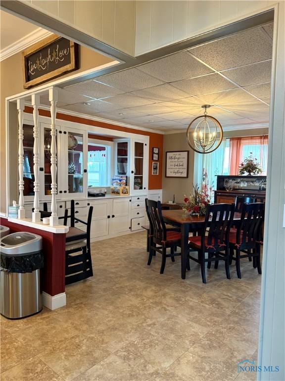 dining area with an inviting chandelier, plenty of natural light, crown molding, and a drop ceiling