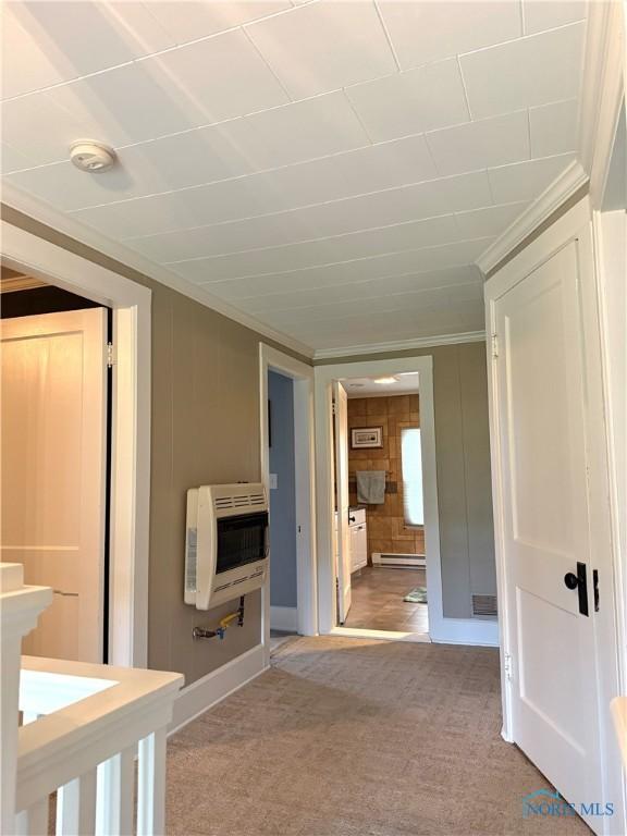 corridor featuring heating unit, crown molding, baseboards, light colored carpet, and a baseboard heating unit