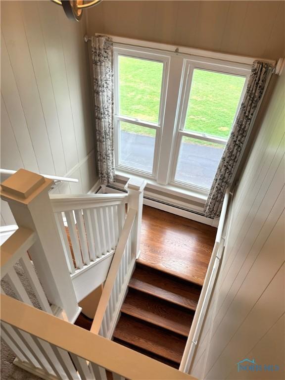 stairs featuring baseboard heating, wood walls, and wood finished floors