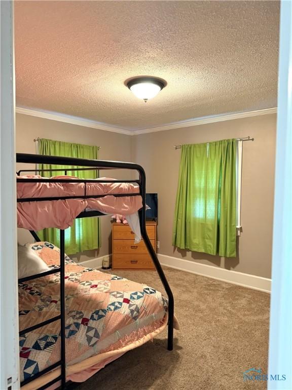 carpeted bedroom featuring baseboards, a textured ceiling, and ornamental molding
