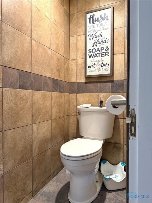 bathroom with toilet, tile patterned floors, and tile walls