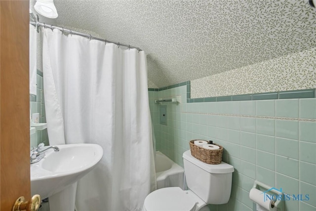 full bathroom with tile walls, shower / tub combo with curtain, toilet, wallpapered walls, and a wainscoted wall