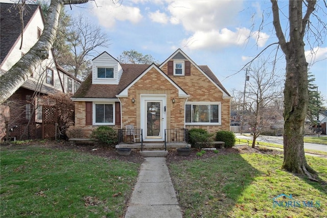 view of front of home featuring brick siding, roof with shingles, and a front yard