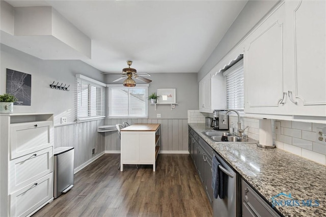 kitchen with a wainscoted wall, a sink, stainless steel dishwasher, dark wood-style floors, and white cabinets