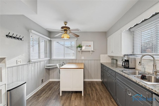 kitchen featuring dark wood-type flooring, a sink, visible vents, a ceiling fan, and wainscoting