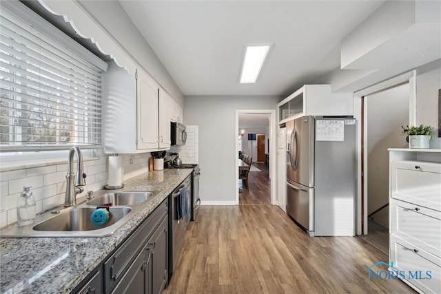 kitchen featuring white cabinetry, stainless steel appliances, decorative backsplash, a sink, and light wood-style flooring