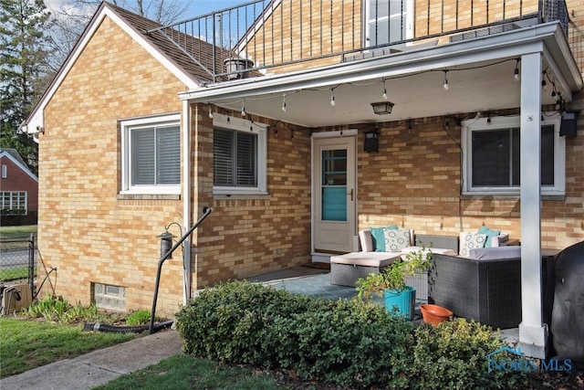 entrance to property featuring a balcony, brick siding, fence, and an outdoor hangout area