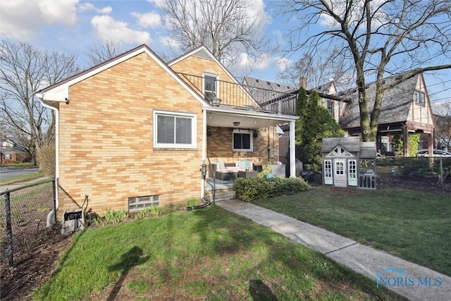 view of front of home with a front yard, an outbuilding, fence, brick siding, and a balcony