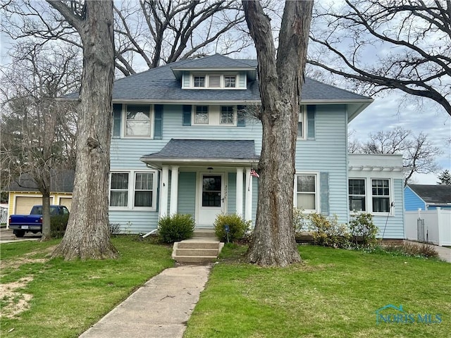 american foursquare style home featuring a front yard, fence, and a shingled roof