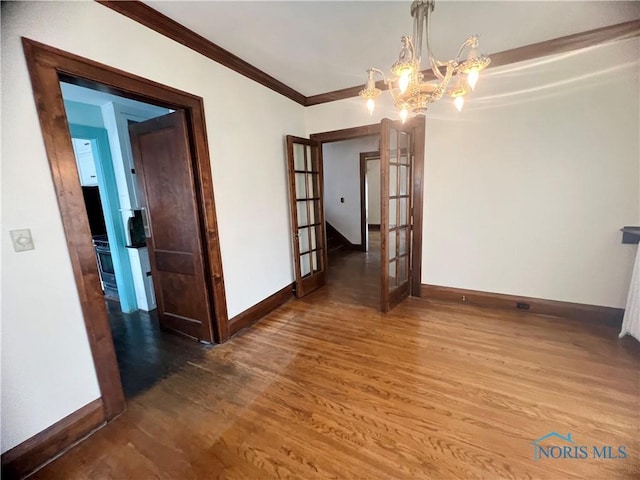 spare room featuring crown molding, wood finished floors, french doors, baseboards, and a notable chandelier