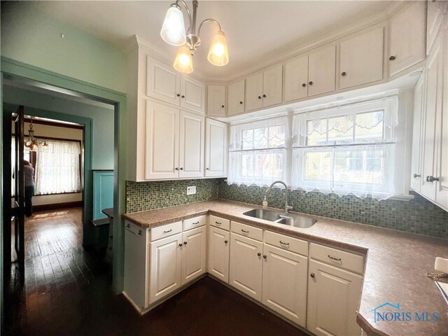 kitchen with a sink, light countertops, dark wood-style floors, white cabinetry, and backsplash