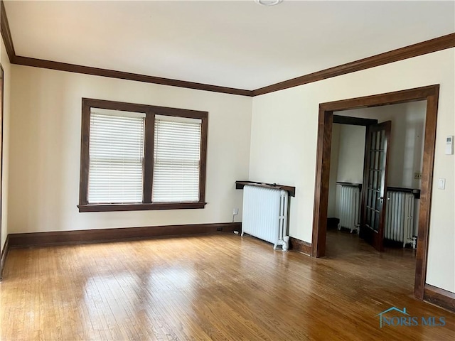 empty room featuring crown molding, baseboards, radiator, and wood finished floors