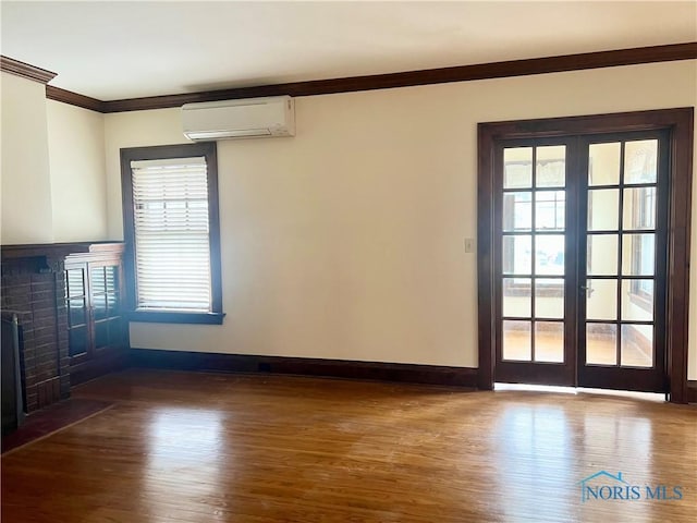 unfurnished living room with plenty of natural light, a wall mounted air conditioner, ornamental molding, a fireplace, and wood finished floors