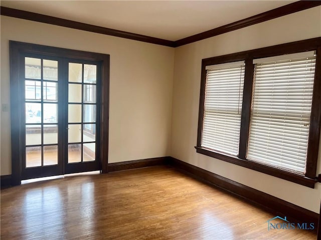 empty room featuring french doors, crown molding, wood finished floors, and baseboards