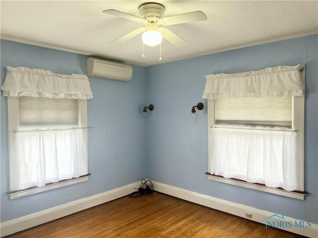 spare room with ceiling fan, baseboards, a wall unit AC, and wood finished floors