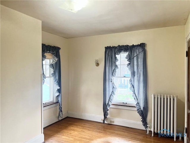 unfurnished room featuring light wood-style flooring, radiator heating unit, and baseboards