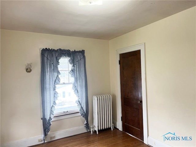 unfurnished room featuring radiator heating unit, baseboards, and dark wood finished floors