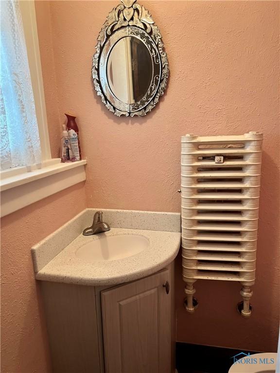 half bath with a textured wall and vanity