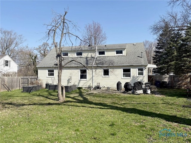 rear view of house featuring roof with shingles, a fenced backyard, and a lawn