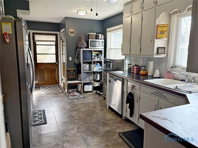 kitchen with appliances with stainless steel finishes, a sink, backsplash, and stone finish flooring