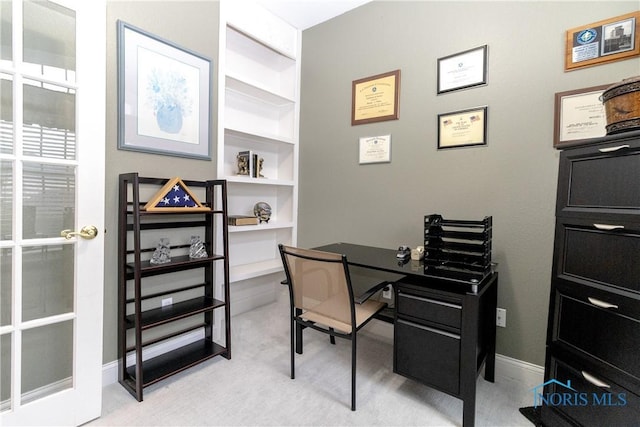 home office featuring baseboards, built in shelves, and light carpet