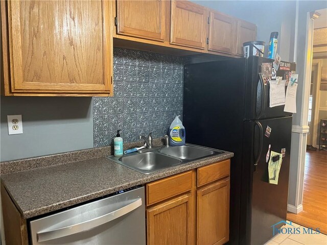 kitchen with a sink, freestanding refrigerator, tasteful backsplash, stainless steel dishwasher, and dark countertops