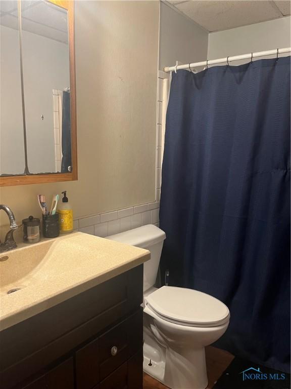 full bathroom featuring a wainscoted wall, toilet, vanity, a shower with curtain, and tile walls