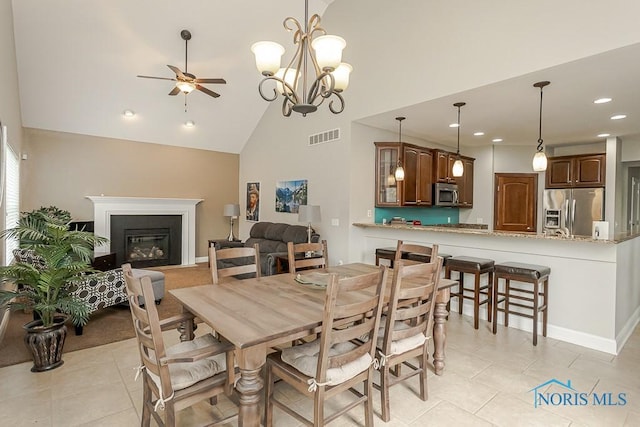 3643 Boulder Ridge Dr, Maumee, OH 43537 - dining room with light tile patterned flooring, a glass covered fireplace, visible vents, ceiling fan with notable chandelier, and high vaulted ceiling