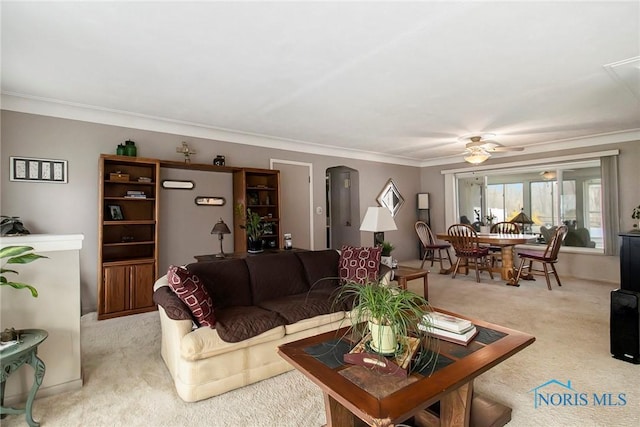 living area featuring crown molding, ceiling fan, arched walkways, and light colored carpet
