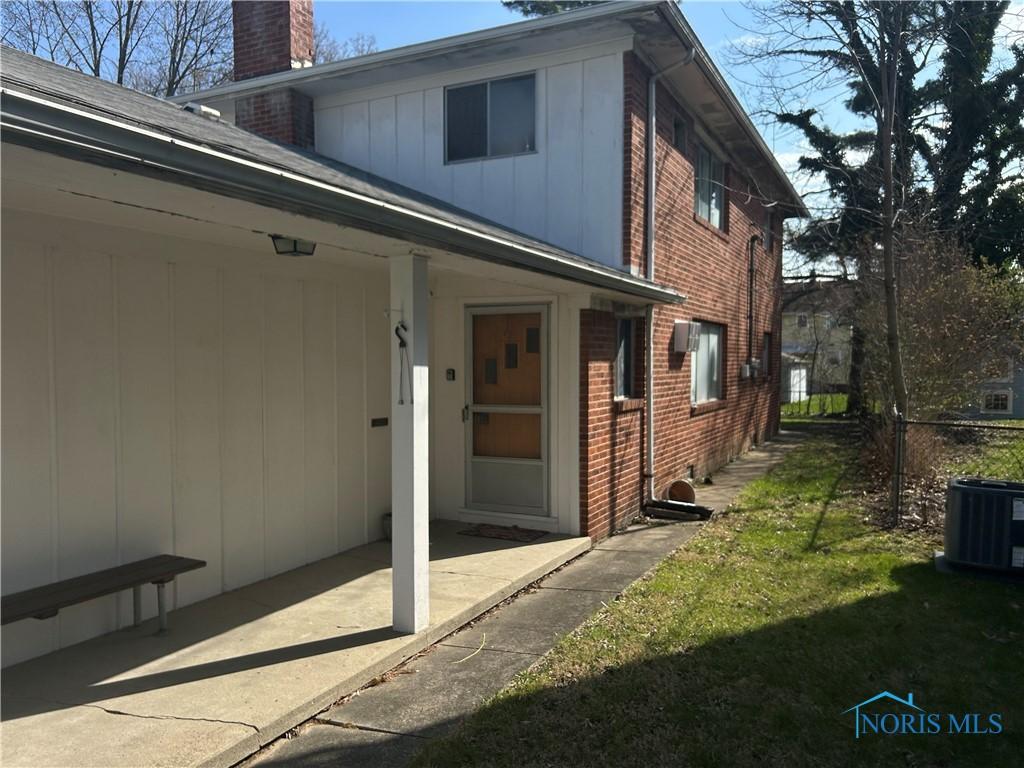 exterior space featuring central air condition unit, a chimney, board and batten siding, brick siding, and a lawn